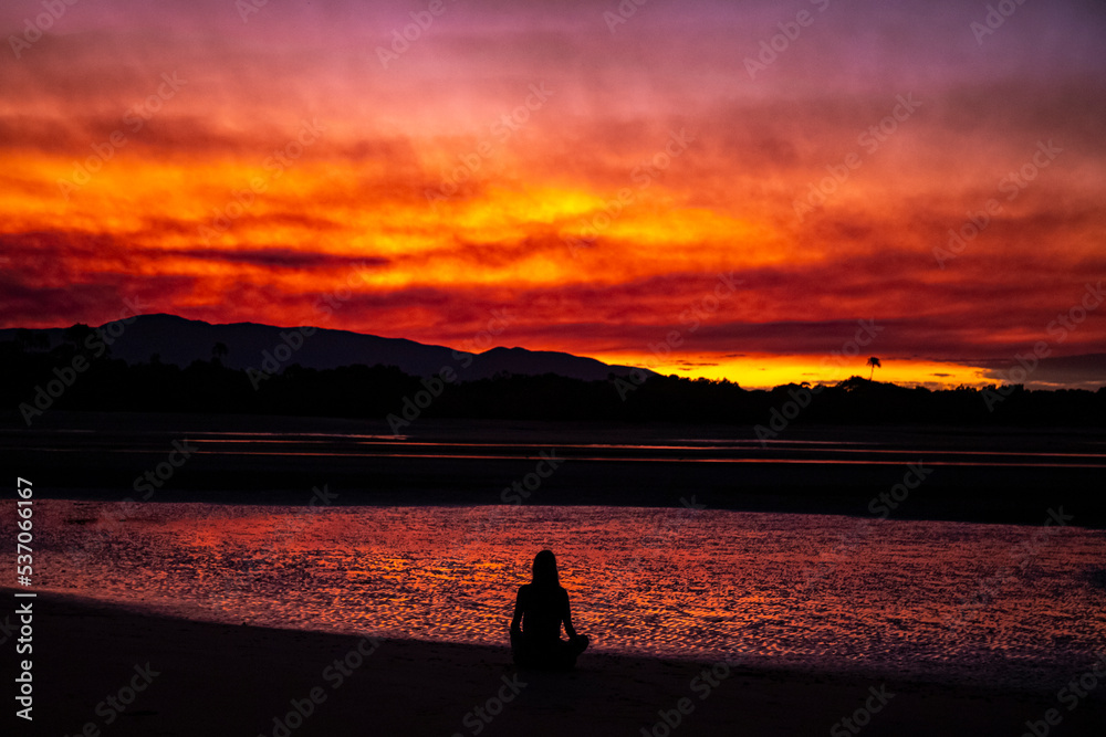 dark silhouette of girl against red sunset on australian beach with palm trees in background, burning sky, red sunset at balgal beach in northern queensland caused by sugarcane burning