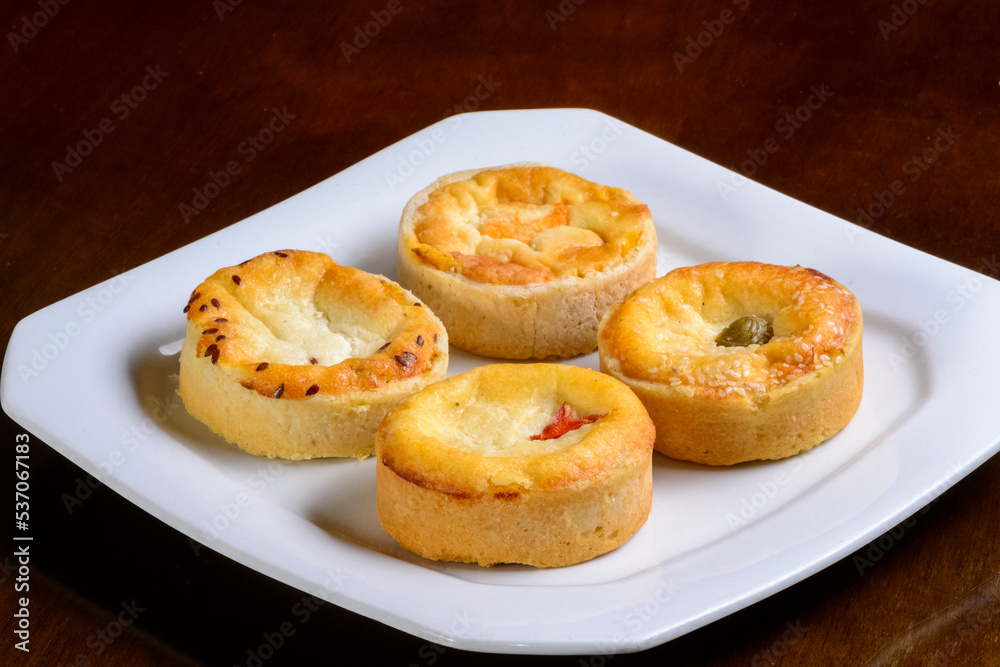 Mini quiches snacks of assorted flavors on a white plate. Mini quiches snacks of assorted flavors on a white plate.