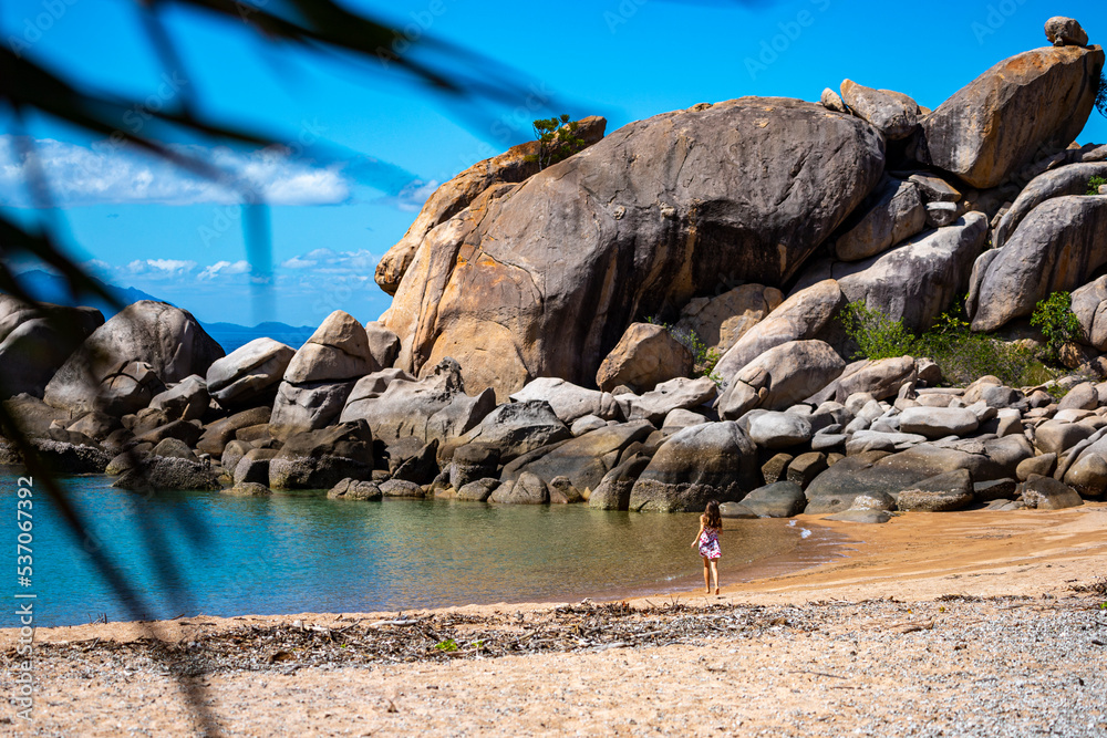 a beautiful long-haired girl in a dress relaxes on a paradise beach on magnetic island; a beach with massive rocks and turquoise water; relaxing on magnetic island, queensland, australia