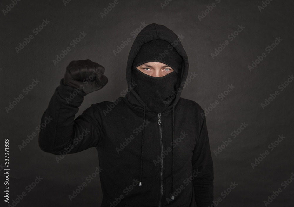 Man in the black hoody with hood wearing balaclava mask with fist up