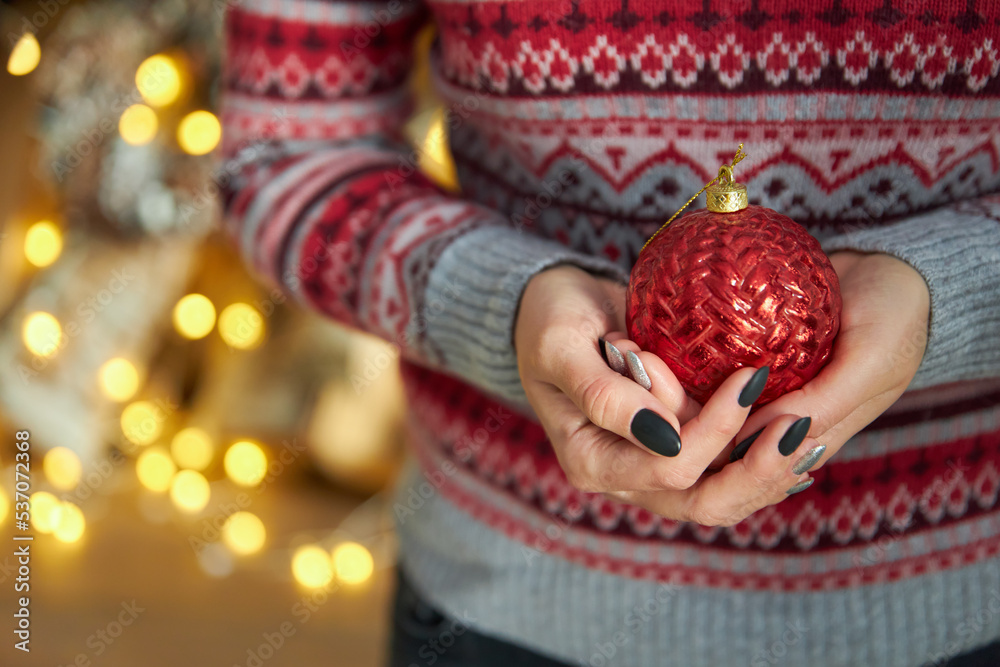 woman in a red striped knitted sweater holds a Christmas ball in her hands. Black manicure on nails