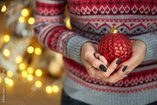 woman in a red striped knitted sweater holds a Christmas ball in her hands. Black manicure on nails