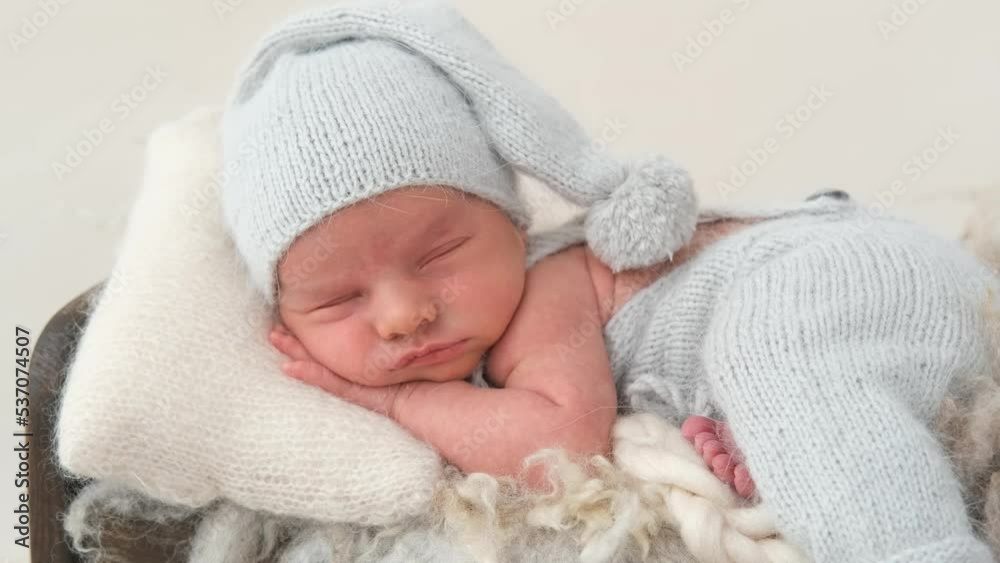 Sweet napping of newborn baby boy wearing knitted pants and hat during professional photoshoot