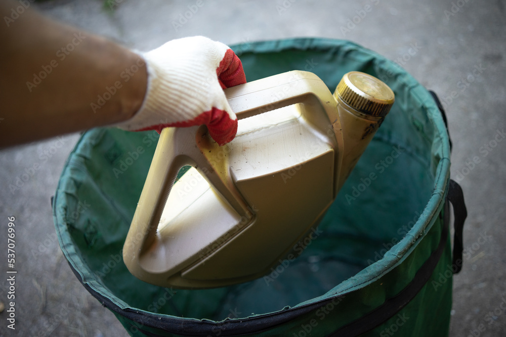 A gloved hand throws out a bottle of engine oil. Disposal of harmful