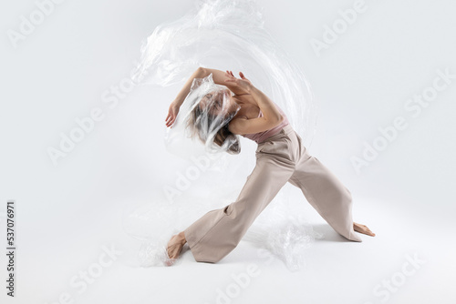 Young beautiful slim girl dances contemporary on a beige studio background