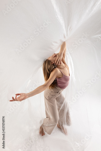 Young beautiful slim girl dances contemporary on a beige studio background