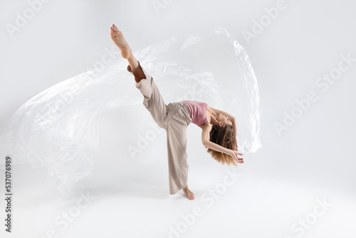 Young beautiful slim girl dances contemporary on a beige studio background