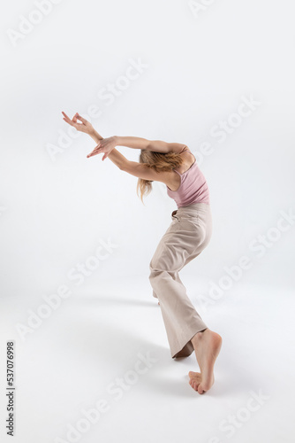 Young beautiful slim girl dances contemporary on a beige studio background