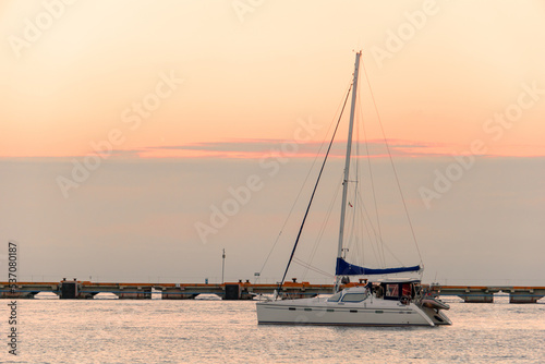 A deserted blurred sailing yacht against a blurred pier and a cloudy sky. Lonely boat at sea during the golden hour at sunset. Boat with a lowered sail, calm.