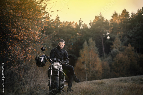 male biker motorcyclist with retro motorcycle in autumn forest.