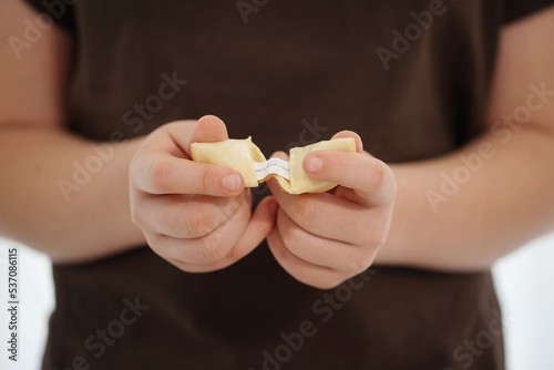 Child holds a fortune cookie in hands with a paper inside
