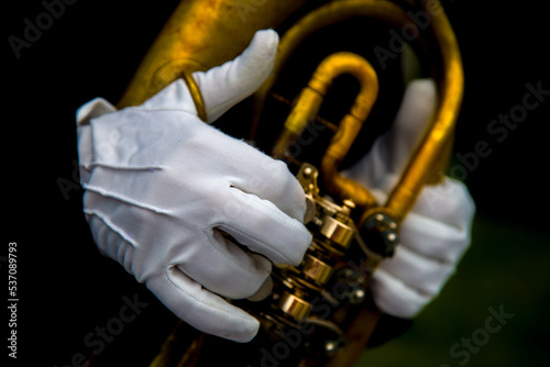 Close-up of the hands of a musician in white gloves playing the baritone tuba on a dark background