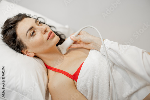 Beautiful adult woman during an ultrasound examination of thyroid gland, lying at medical office. Endocrine system health concept photo