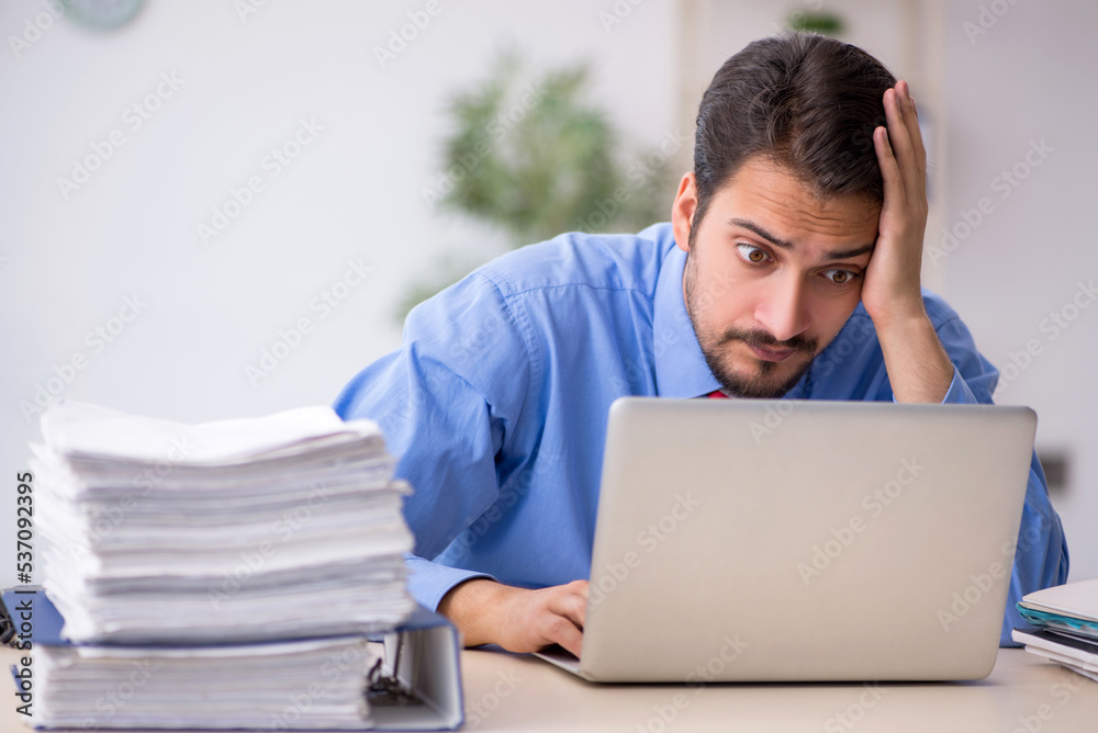 Young male employee unhappy with excessive work in the office Young male employee unhappy with excessive work in the office