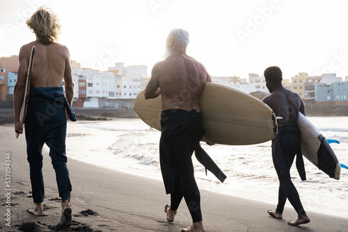 Diverse surfer friends holding surf boards after water sport session with beach on background - Focus on right guy back
