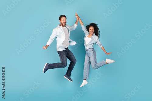 Excited cheerful millennial caucasian and arabic couple jumping in air, give high five, on free space