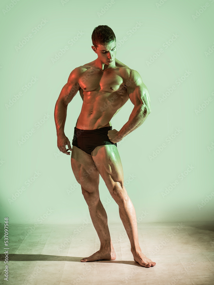 Handsome bodybuilder doing classic double biceps pose, looking away, on dark background Handsome bodybuilder doing classic double biceps pose, looking away, on dark background