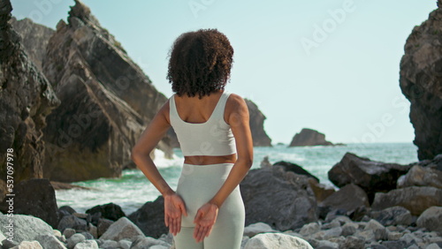 Girl making Namaste hands behind back on rocky seashore. Woman stretching arms.