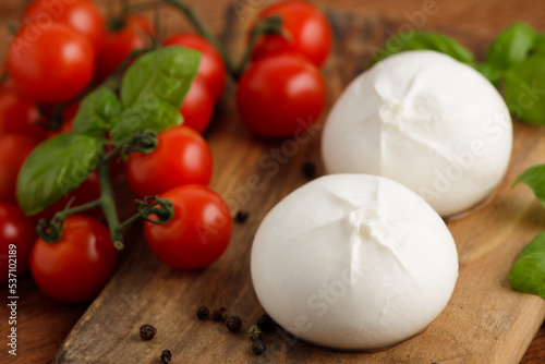 Fresh Italian burrata with tomatoes and basil on wooden cutting board, close up. Burrata cheese ball made from mozzarella and cream. Healthy food