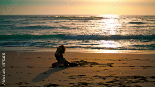 Girl performing sensual dance on sand beach at sunrise. Silhouette woman dancer.