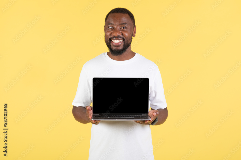 Happy African American Guy Showing Laptop Screen Over Yellow Background Happy African American Guy Showing Laptop Screen Over Yellow Background