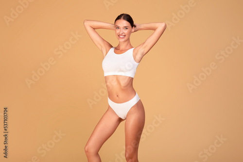 Slim lady with perfect body and flat stomach posing on beige studio background, woman wearing white top bra and panties © Prostock-studio