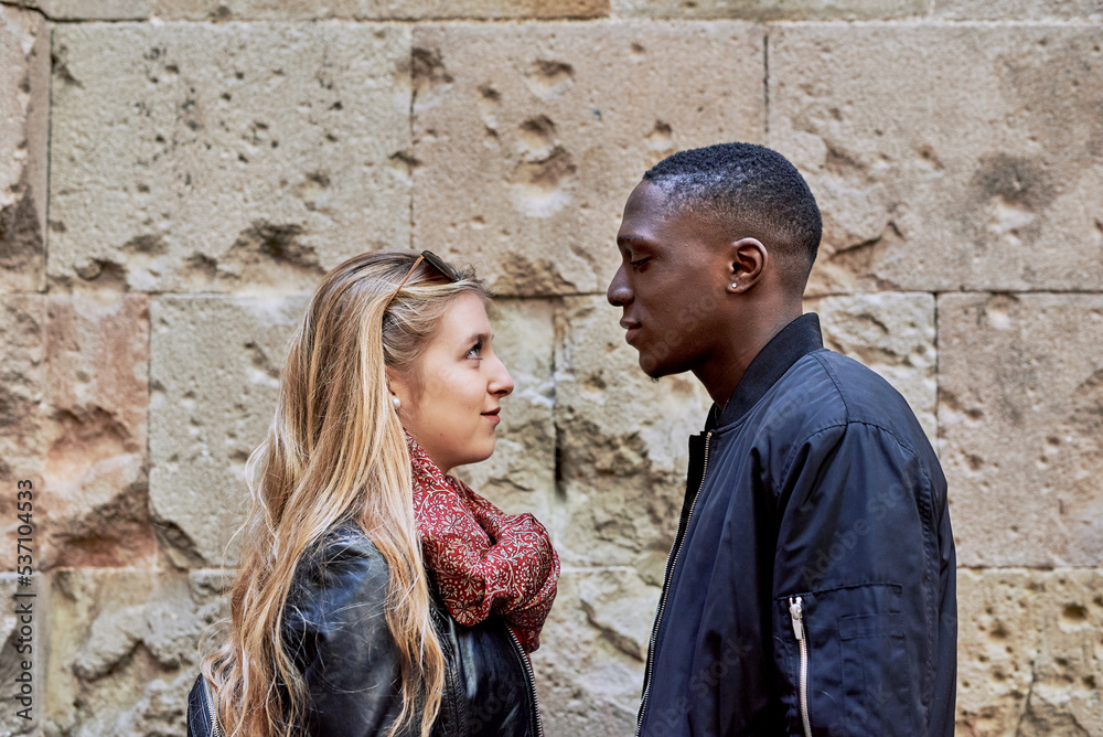 Smiling couple looking face to face against stone wall.