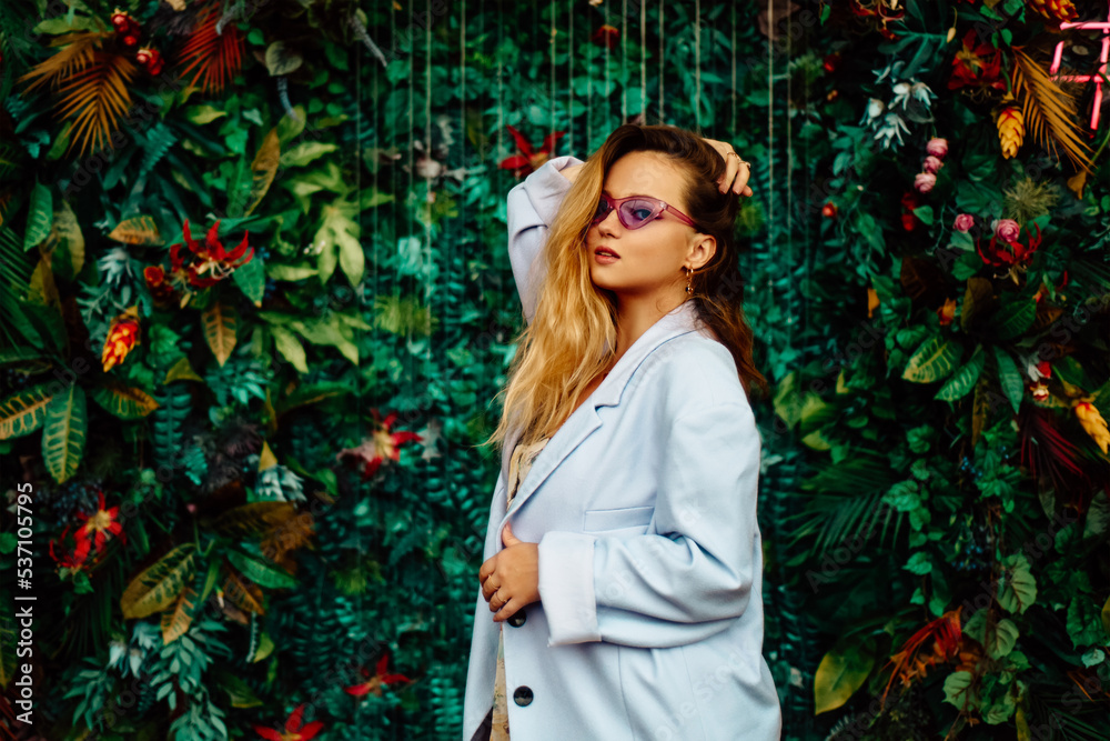 A girl in a dress, jacket and purple sunglasses poses at the festival portrait. Smile and joy, emotions against the backdrop of greenery and a waterfall. fashion outfit.