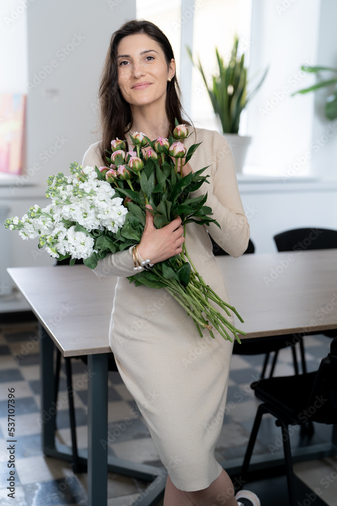 Positive woman holding a huge bouquet of flowers in her office. Birthday present smile. Positive woman holding a huge bouquet of flowers in her office. Birthday present smile.