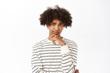 Close up portrait of hispanic guy with curly hair thinking, looking bothered by dilemma, pondering, standing over white background