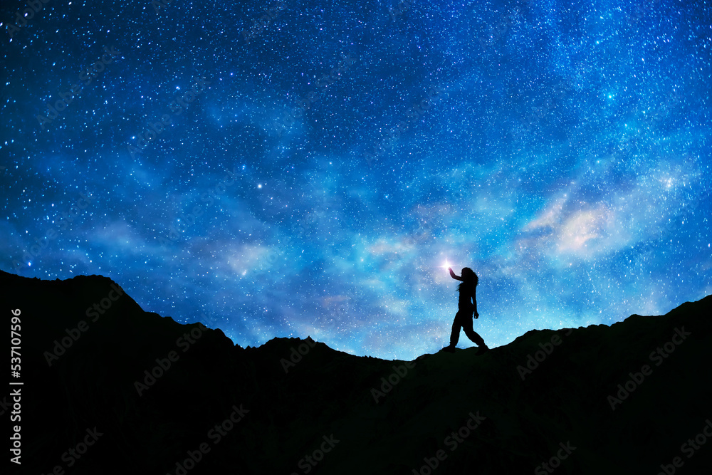 Girl silhouette stands on the hill on and looks on the  milky way galaxy. Dark starry night.