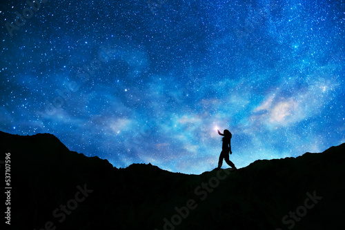 Girl silhouette stands on the hill on and looks on the milky way galaxy. Dark starry night.