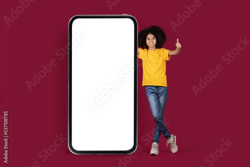 Cool african american child girl standing by big smartphone, mockup