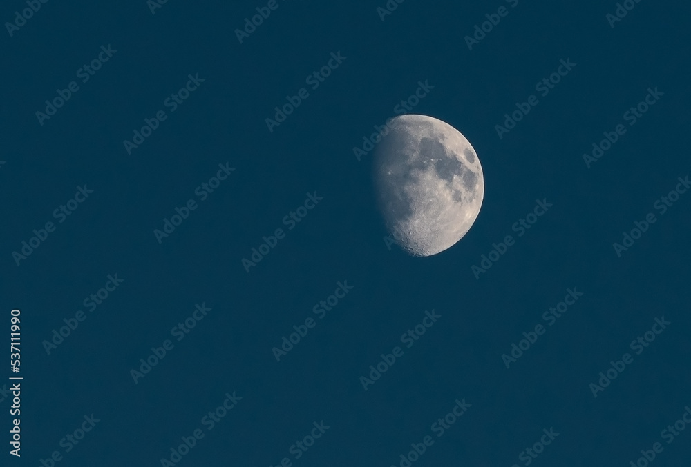 A white moon with clearly visible craters in a blue evening sky.