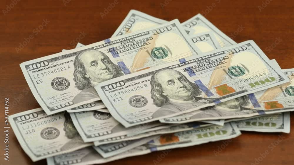 One hundred dollar bills USD cash falling in fast motion onto a table top, forming a loose pile One hundred dollar bills USD cash falling in fast motion onto a table top, forming a loose pile