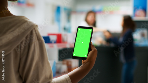 Female client holding smartphone with greenscreen display in pharmacy retail store, using isolated mockup template. Looking at blank chroma key copyspace in drugstore, buying medicine.