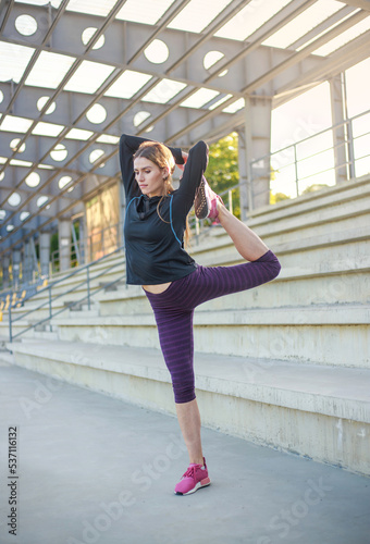 Young woman in concrete public stadium doing fitness stretching exercises, sports and healthy lifestyle
