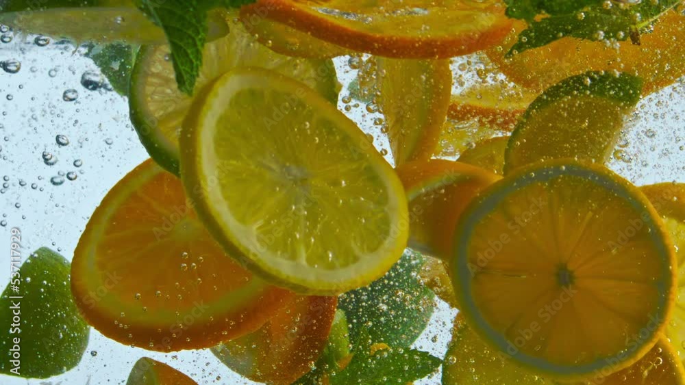 Pieces citrus fruit dropped with mint in water closeup. Sliced orange lemon lime