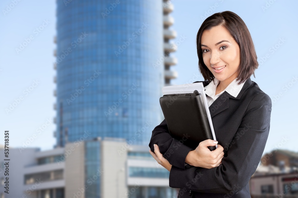 Smiling business woman holding papers on city background Smiling business woman holding papers on city background