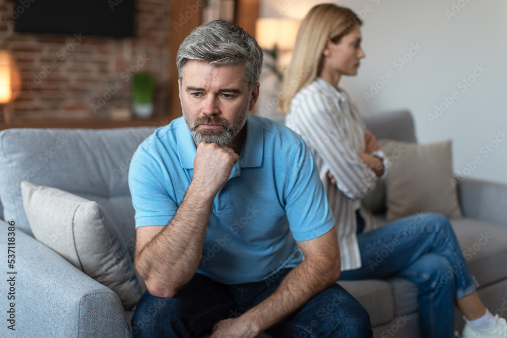 Unhappy middle aged european man ignores offended lady after quarrel in living room interior