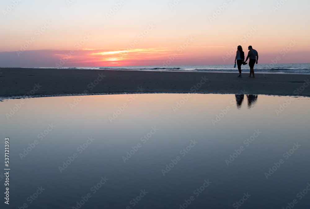 Couple walking at sunrise on Coligny Beach, Hilton Head Island, South Carolina.