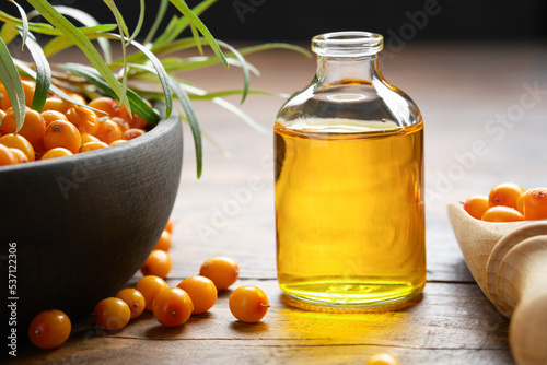 Bottle of sea buckthorn essential oil, bowl of sandthorn berries, wooden scoop of sea buckthorn berries.