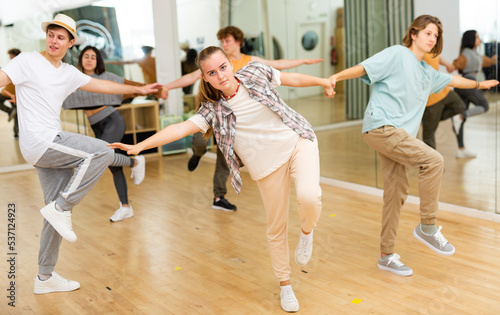 Interested modern teen girl practicing dynamic boogie-woogie in pair with boy during group class in dance studio for youth.