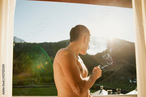 Shirtless guy smoking a marijuana joint on the terrace in the morning photo