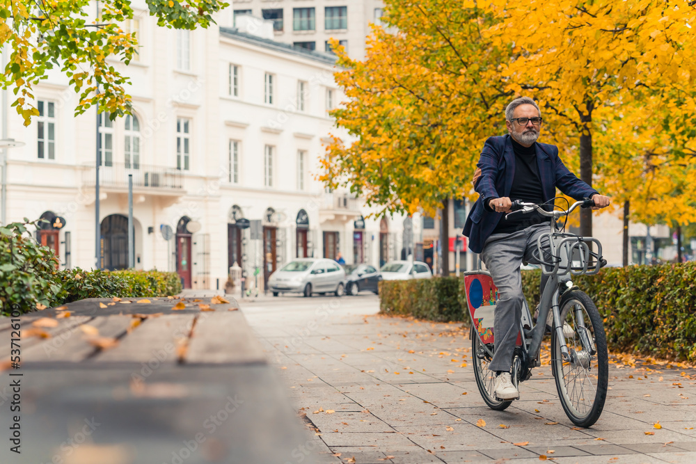 Fall outdoor activities. Full-length shot of middle-aged caucasian bearded man in business casual clothing riding a rented bike. Autumn in the city. High quality photo