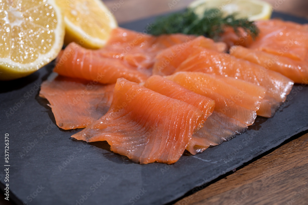 Slices of tasty smoked Scottish salmon fish served on black plate with lemon and fresh dill Slices of tasty smoked Scottish salmon fish served on black plate with lemon and fresh dill