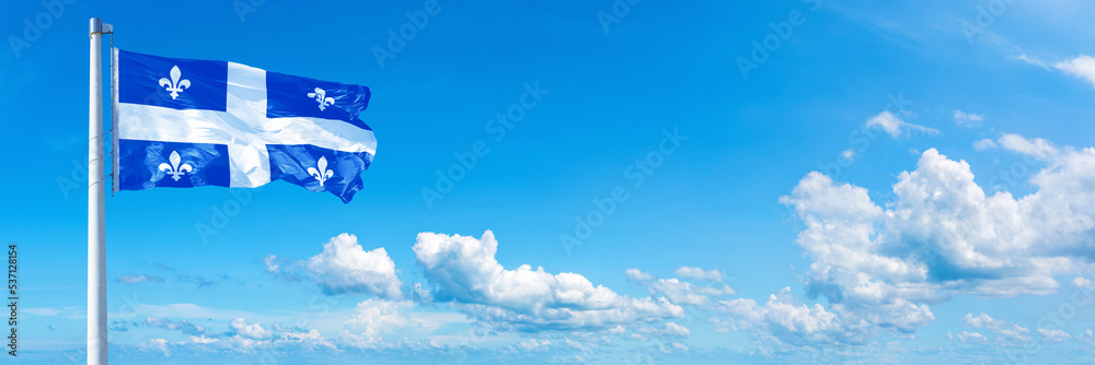 Fototapeta premium Quebec - Canada flag waving on a blue sky in beautiful clouds - Horizontal banner 