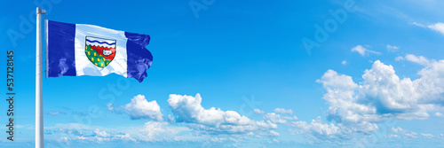 Northwest Territories - Canada flag waving on a blue sky in beautiful clouds - Horizontal banner
