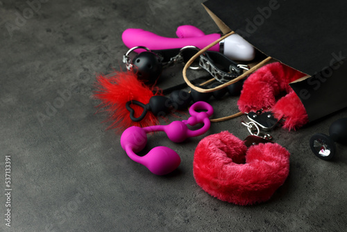 Paper shopping bag with different sex toys on grey table. Space for text