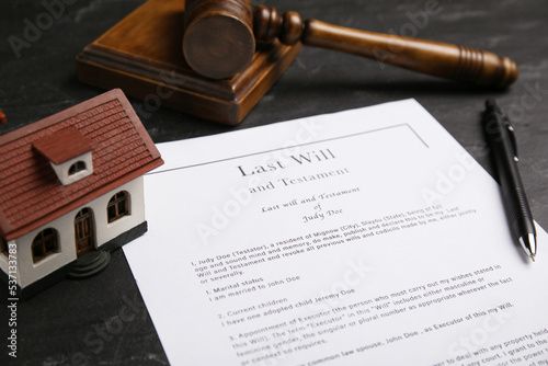 Last will and testament near house model, pen, gavel on black table, closeup